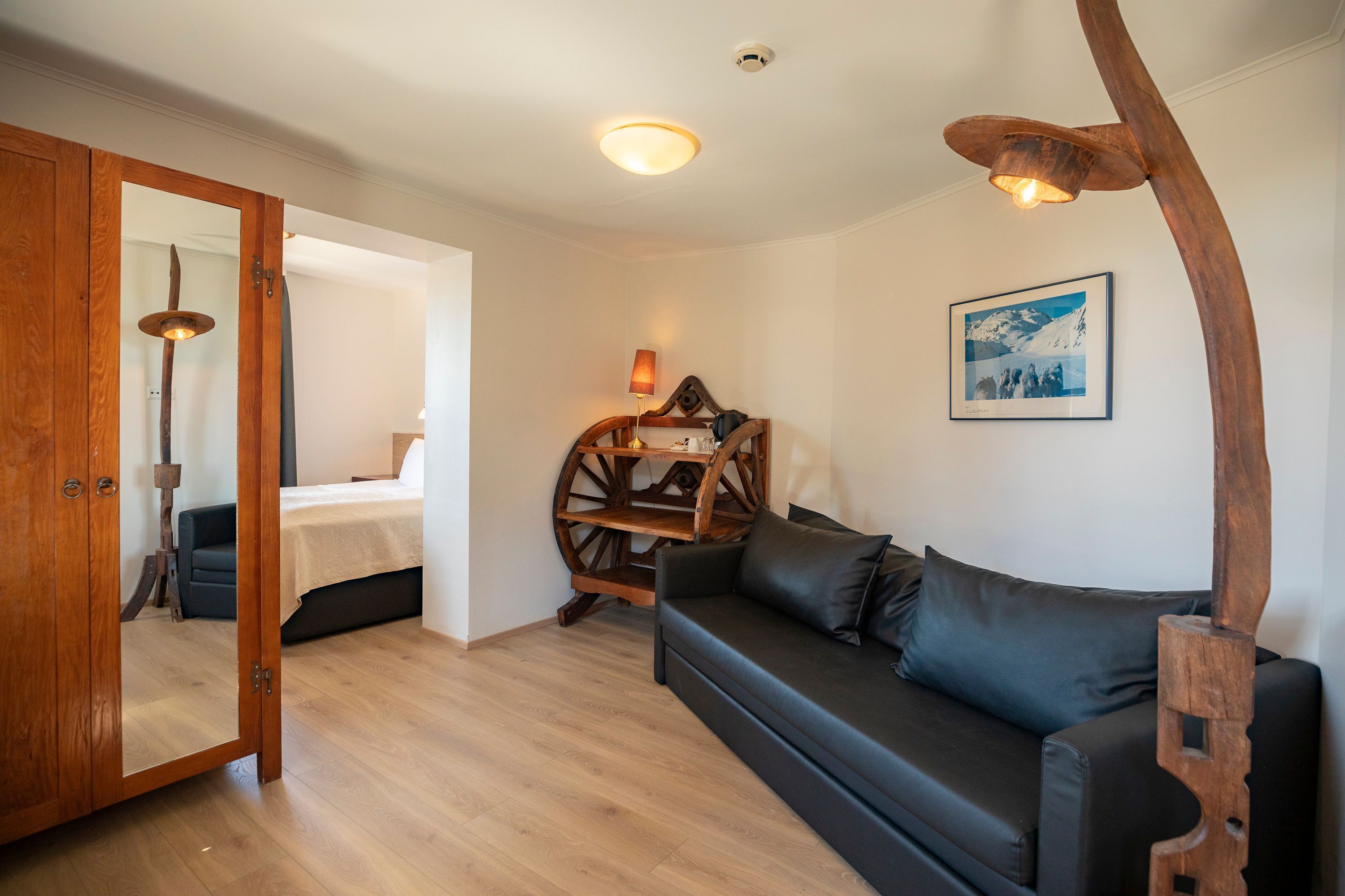 A cozy room with a wooden door, a bed, a black leather sofa, a wooden side table, and a wall-mounted picture.