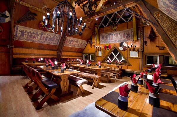 Un interior rústico de madera con varias mesas y bancos de madera, una araña y decoraciones en las paredes.