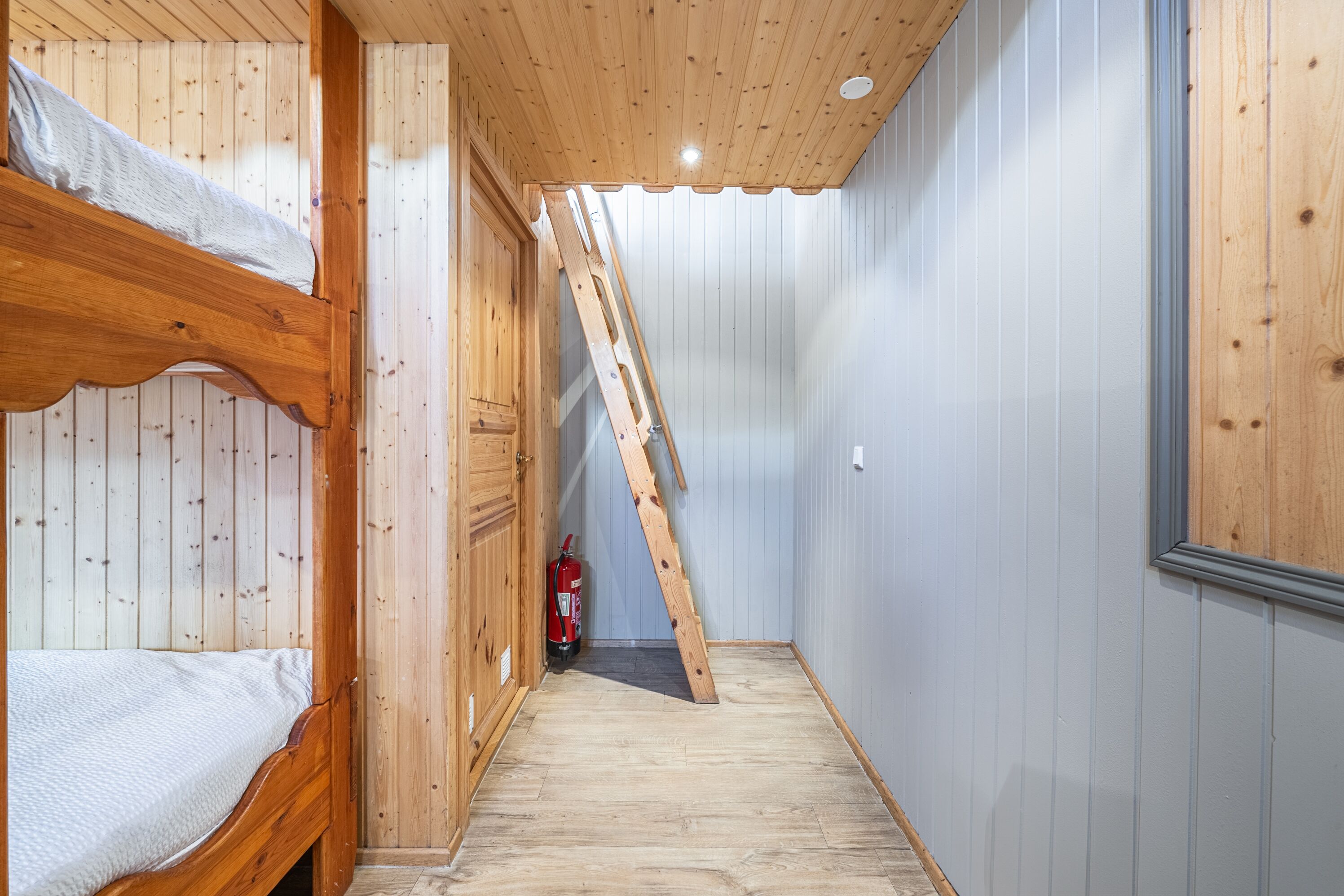 Habitación con literas de madera y escalera que lleva a un altiloque.