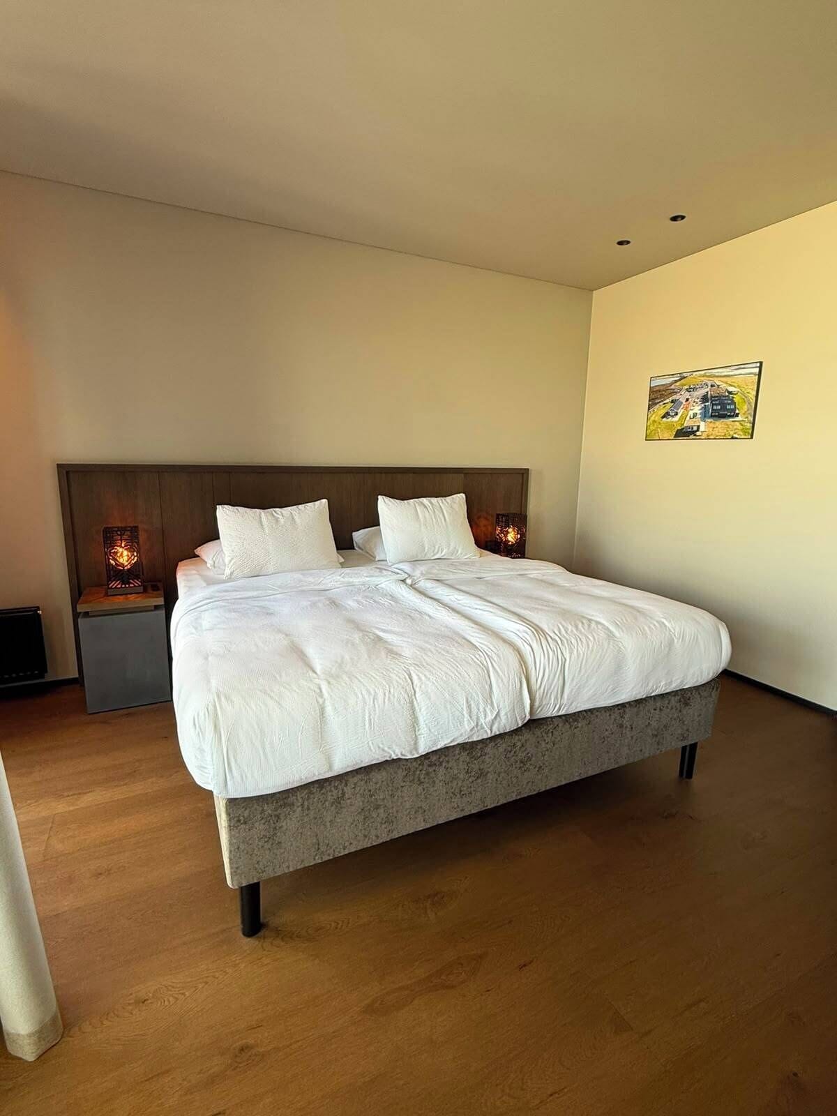 A modern bedroom with a large bed, wooden headboard, and a nightstand with a lamp.