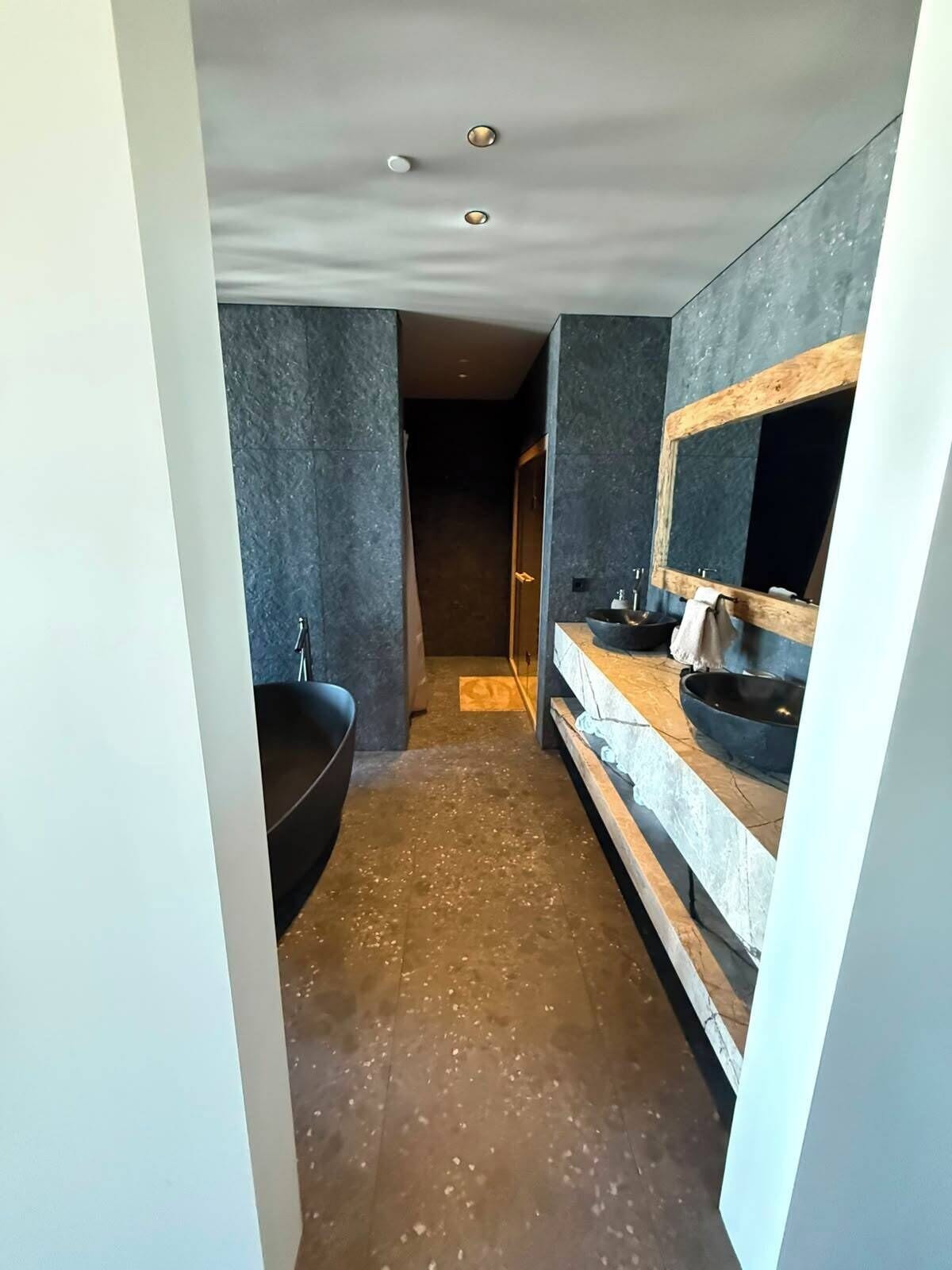 Un baño moderno con una bañera independiente, un espejo grande y un mueble de tocador de madera.