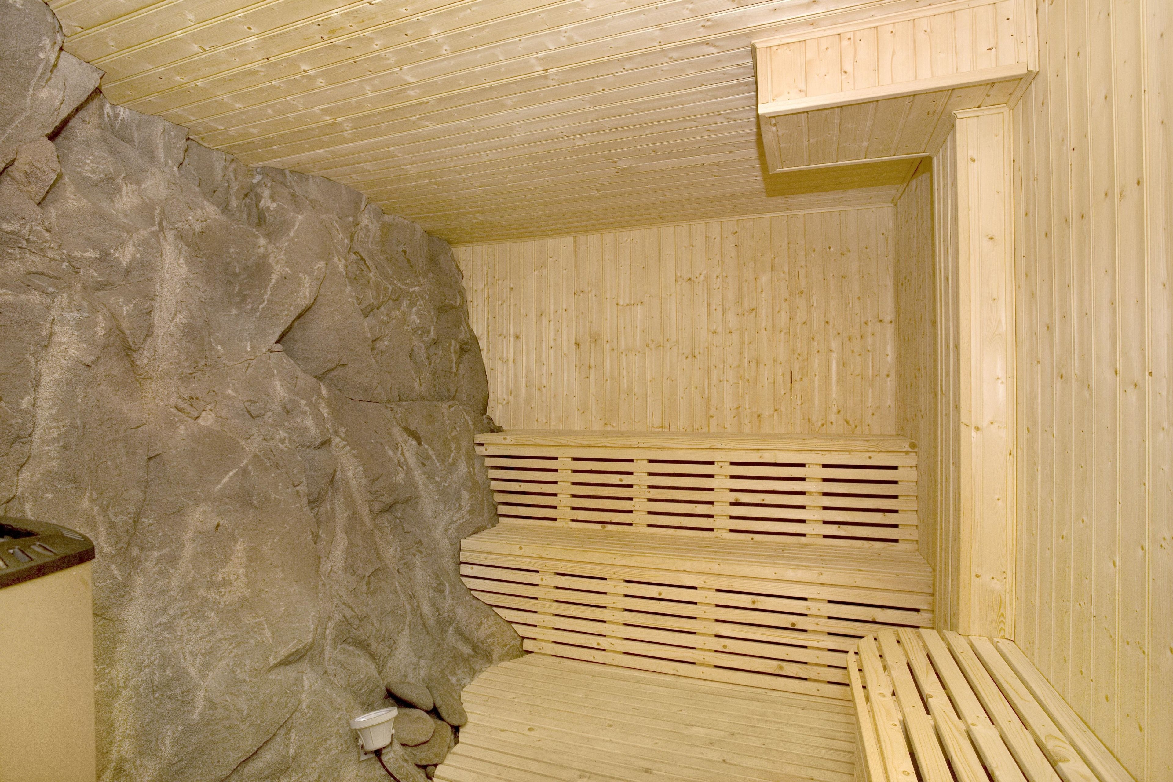A sauna with wooden benches, a stone wall, and a wooden ceiling.