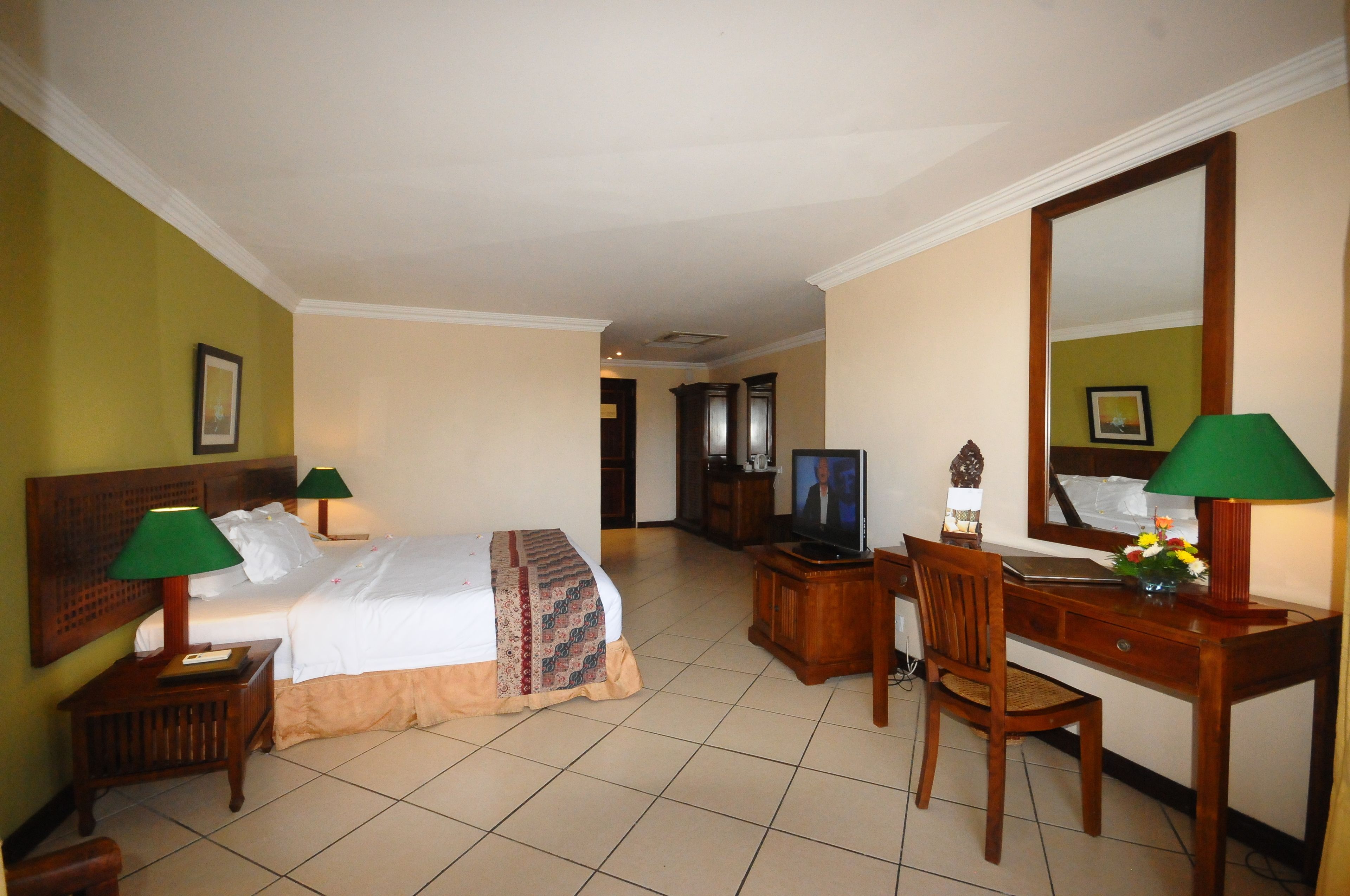 Habitación de hotel con cama, escritorio, silla, televisión y espejo.