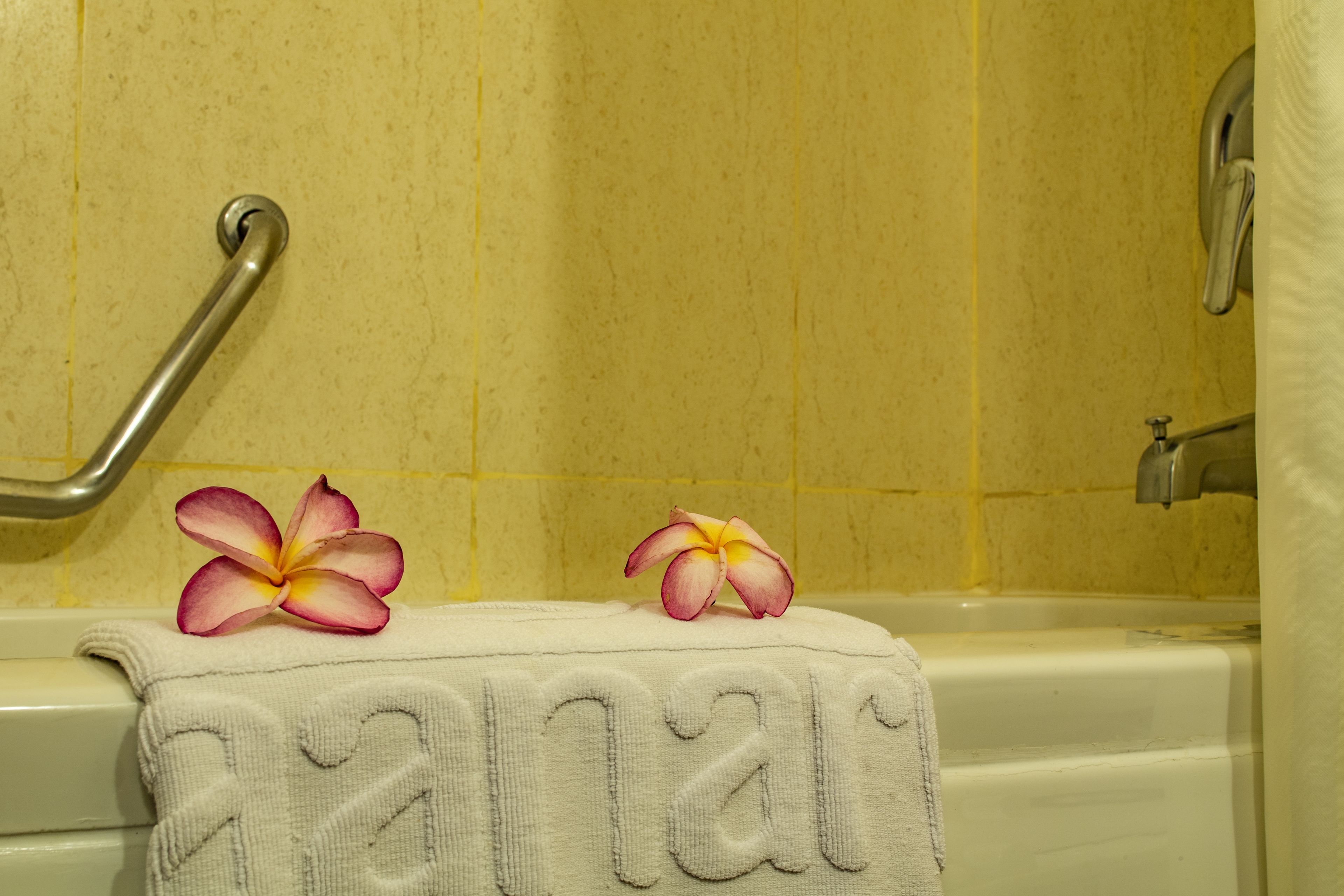 Un baño con una bañera, una toalla con diseño de corazón y dos flores sobre la toalla.