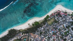 An aerial view of a coastal area with a beach, a marina, and a residential area with buildings and roads. - Aanari Hotel and Spa (Flic-en-Flac)