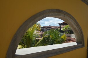 Vista a través de una ventana de arco de piedra sobre un patio con palmeras y edificios.