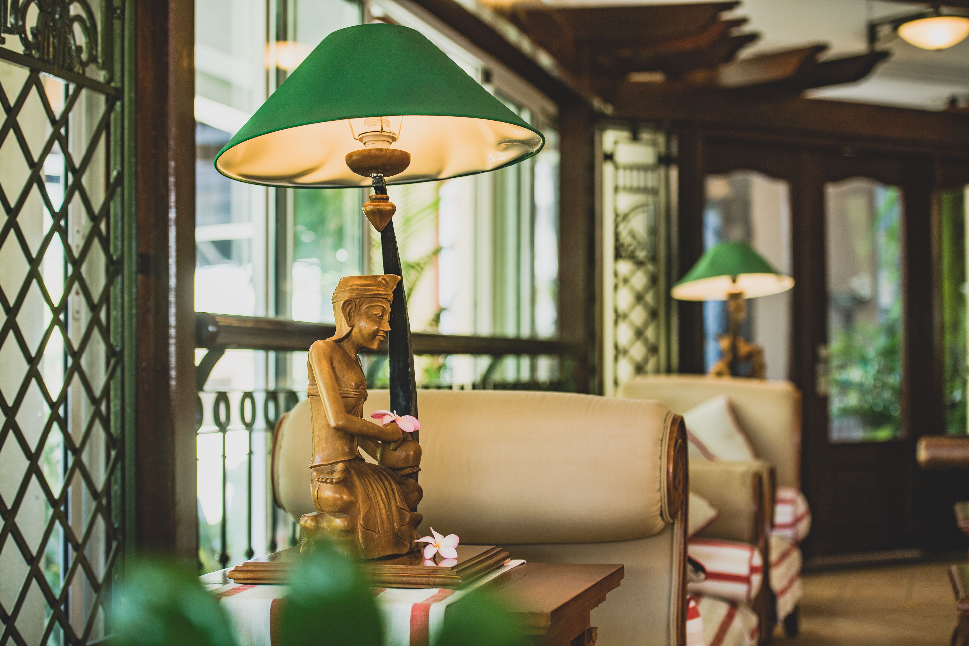 A statue of a woman holding a flower, a green lamp, and a sofa in a room with wooden beams and a lattice window.