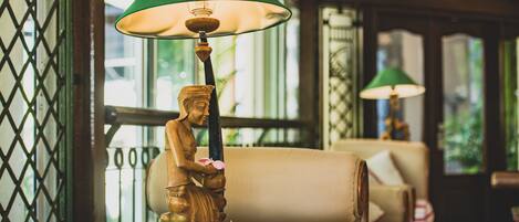 A statue of a woman holding a flower, a green lamp, and a sofa in a room with wooden beams and a lattice window.