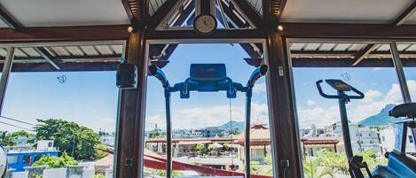Un gimnasio con cinta de correr, bicicleta estática y vistas de la ciudad a través de amplias ventanas.