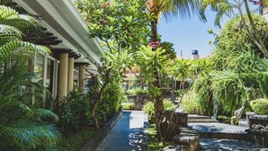 A lush garden pathway with a stone water feature, surrounded by tropical plants and palm trees. - Aanari Hotel and Spa (Flic-en-Flac)