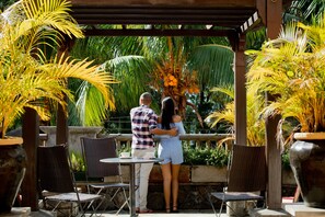 Relax in a serene outdoor space surrounded by lush tropical plants and a shaded pergola.