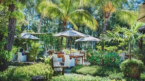 An outdoor seating area with tables and chairs, surrounded by lush greenery and palm trees. - Aanari Hotel and Spa (Flic-en-Flac)