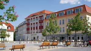 Un hotel con fachada roja y blanca, mesas al aire libre y una plaza adoquinada.