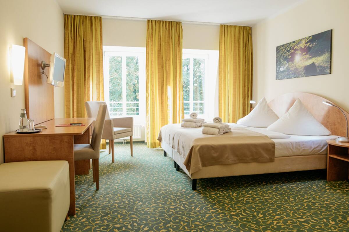 A hotel room with a bed, a desk, a chair, and a window with curtains.