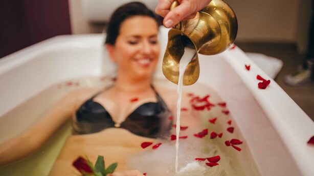 Una persona en una bañera con pétalos de rosa y un grifo dorado.