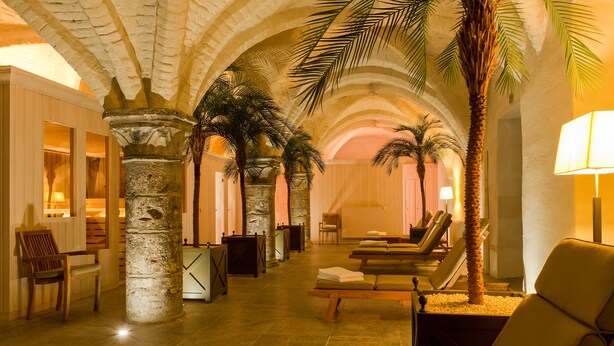 Un espacio de spa con pilares de piedra, palmeras y sillones de descanso.