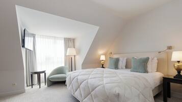 Una habitación de hotel moderna con una cama grande, dos mesitas de noche, una silla y una ventana con cortinas.