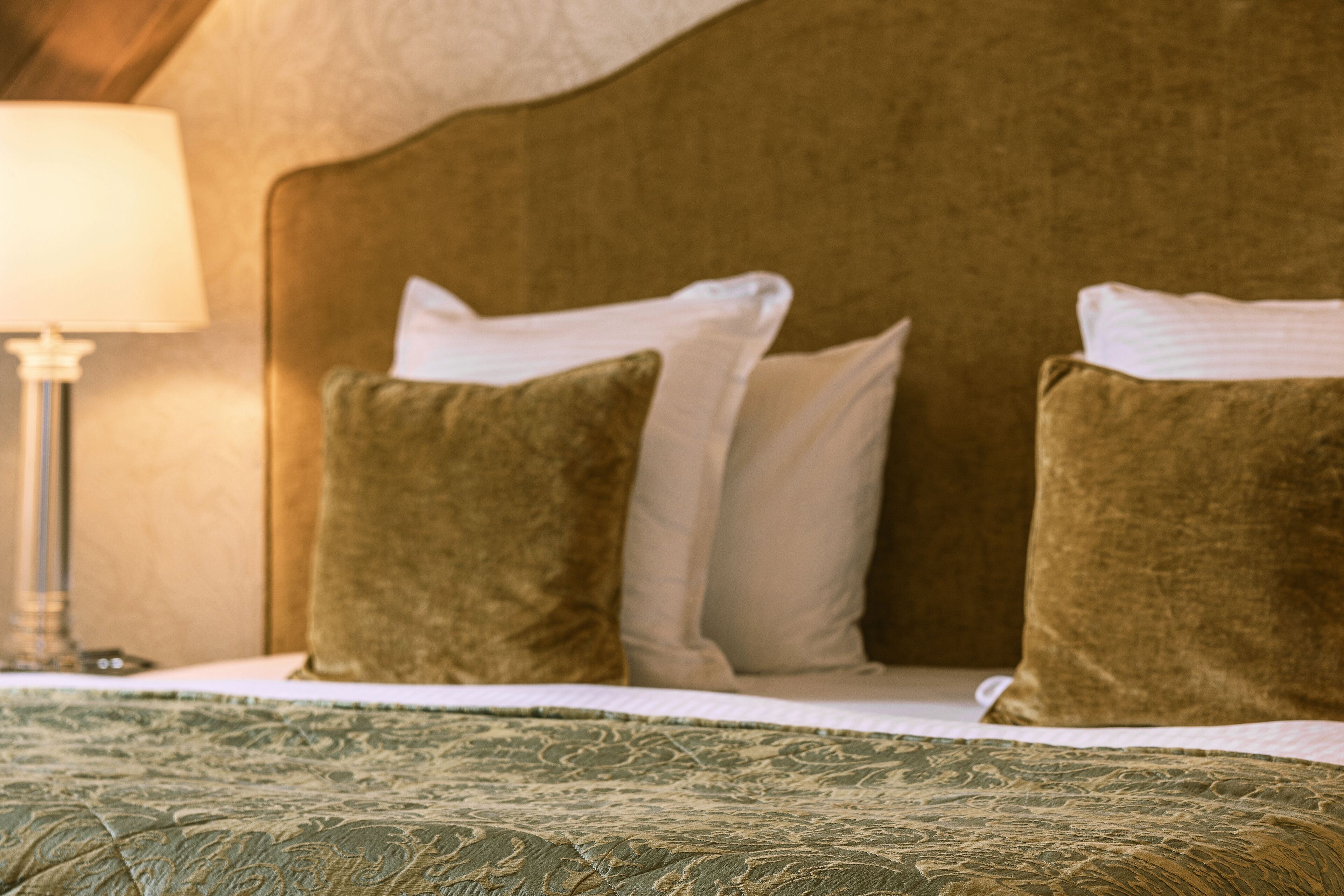 A bed with a green patterned bedspread, two pillows (one green, one white), and a bedside lamp.
