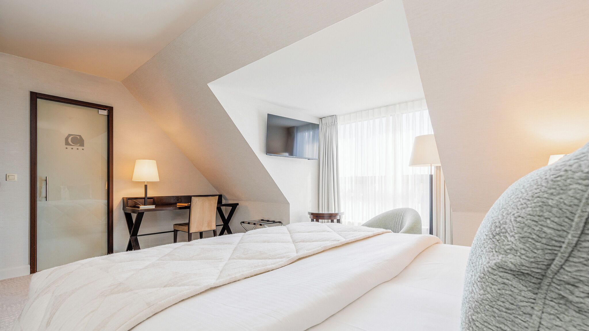 Une chambre d’hôtel avec un lit, un bureau, une chaise, une télévision et une fenêtre avec des rideaux.