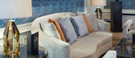 A plush sofa with multiple pillows, a glass coffee table, and a lamp.