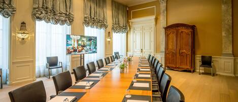 A conference room with a long table, chairs, and a television screen.