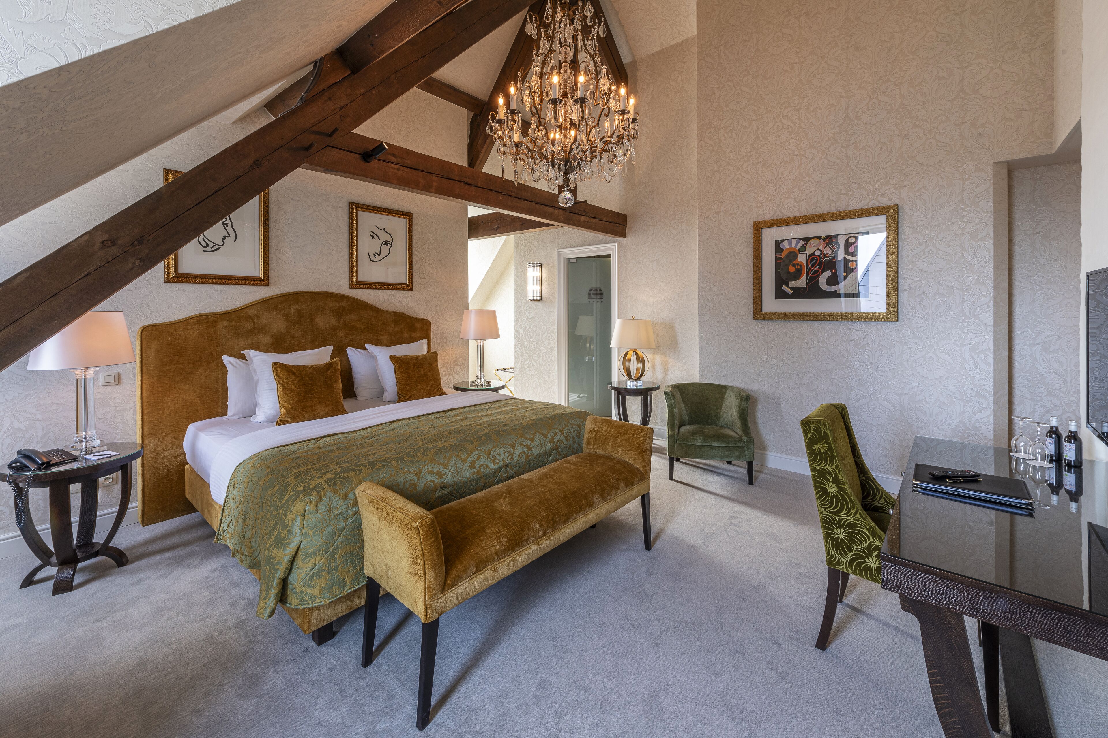 A spacious bedroom with a large bed, a bench, a dining table, and a chandelier.