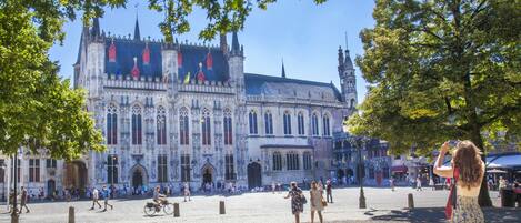 Un bâtiment historique à l’architecture complexe, une place pavée et des gens qui se promènent.