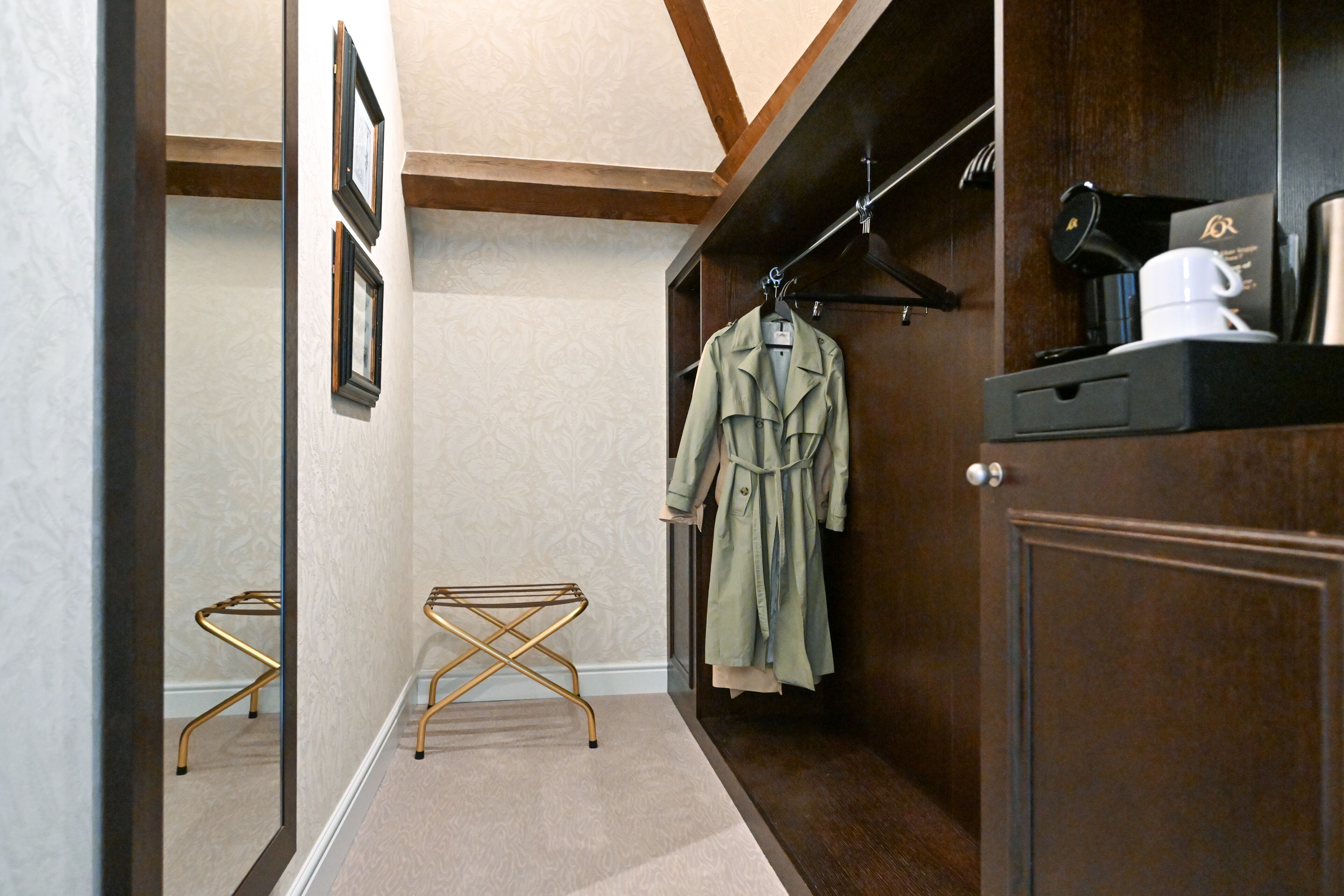 A hallway with a wooden wardrobe, a coat rack with a green coat, a coffee machine, and a small table with a gold stand.