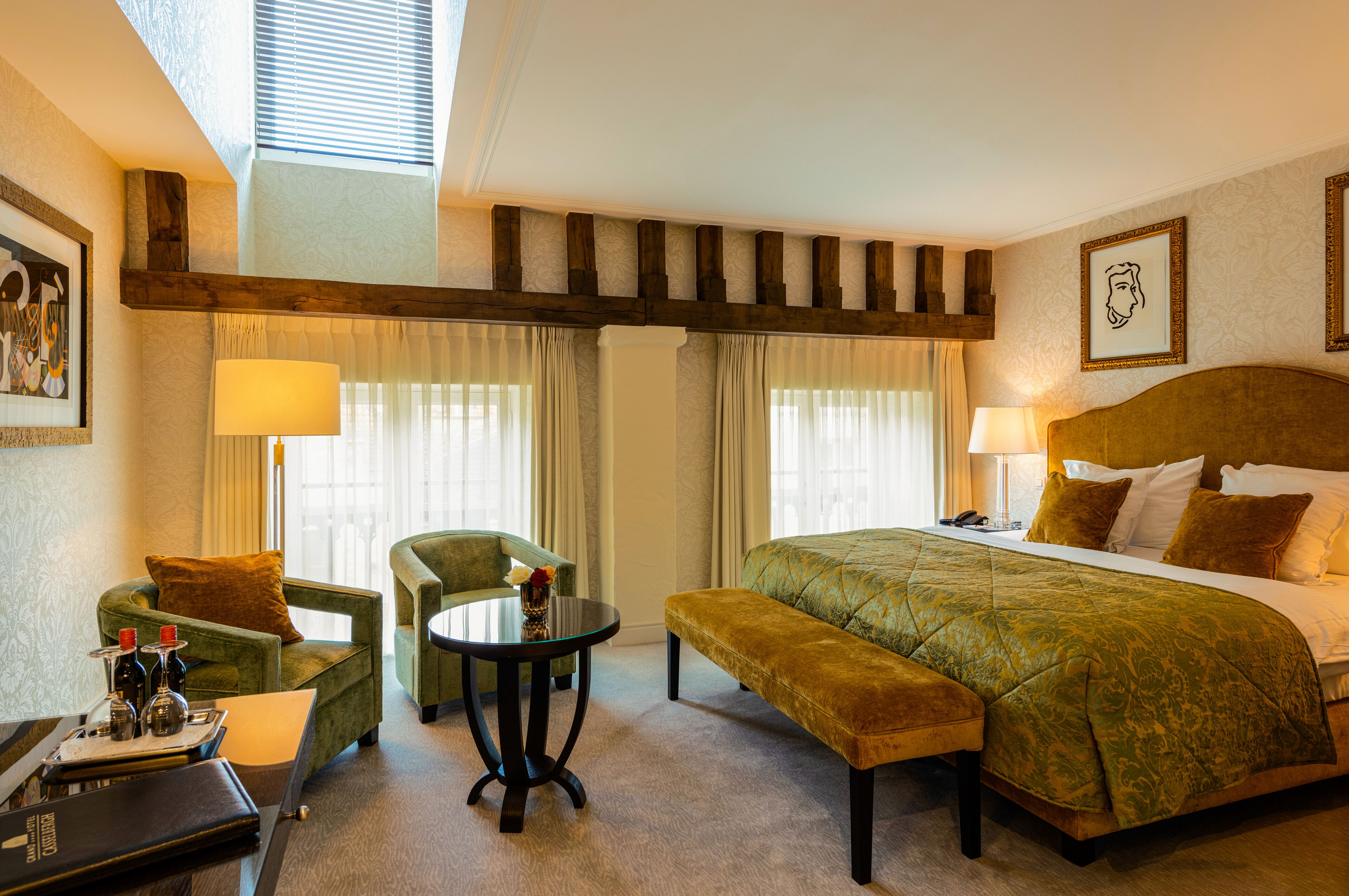 A hotel room with a large bed, a green sofa, a round table, and a bench.