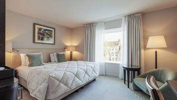 A hotel room with a large bed, a desk, a chair, a lamp, and a window with curtains.