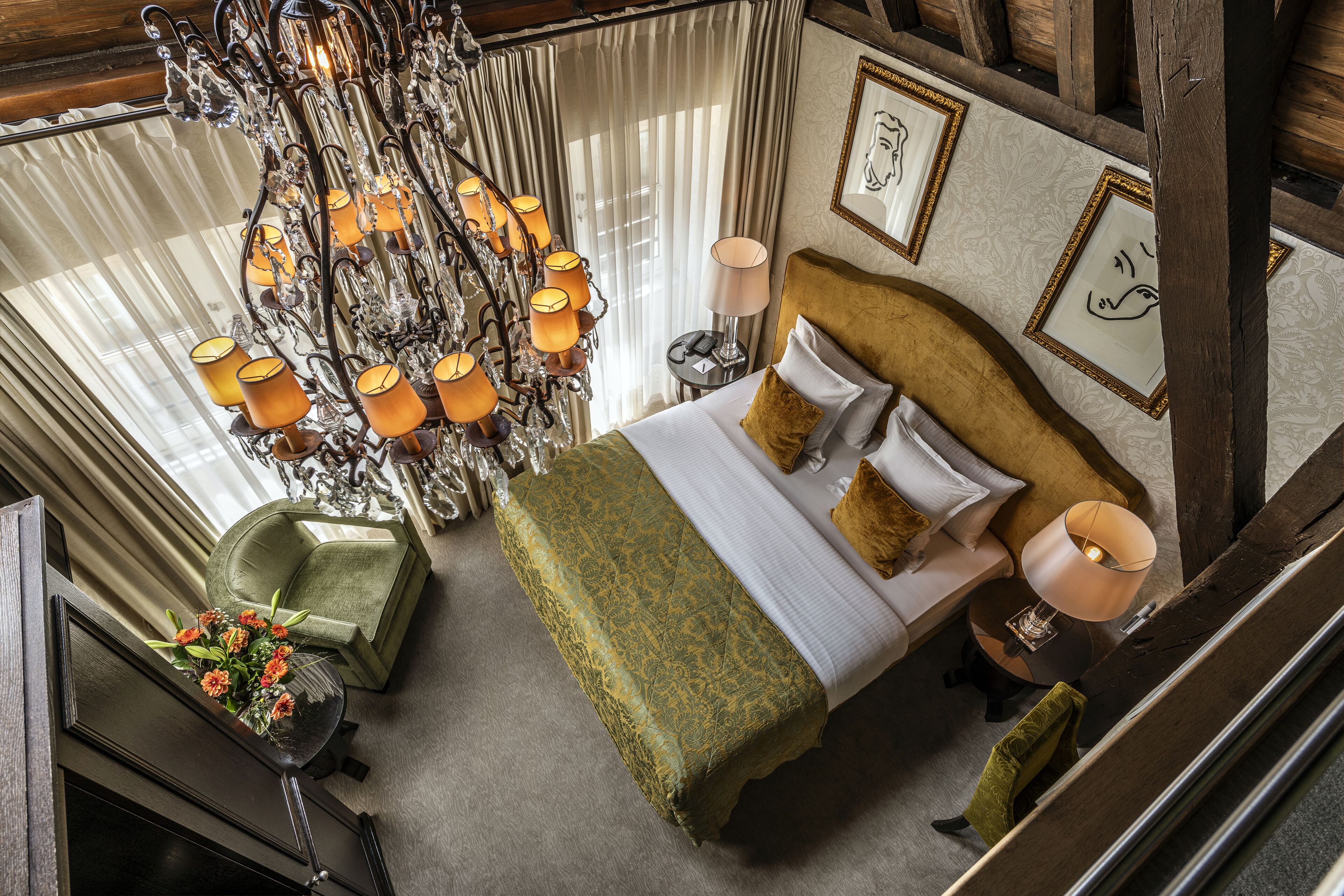 A high-ceilinged room with a large bed, a chandelier, and a view of the outdoors.