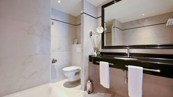 Un baño moderno con inodoro blanco, bañera, un espejo grande y una encimera negra con toallero.