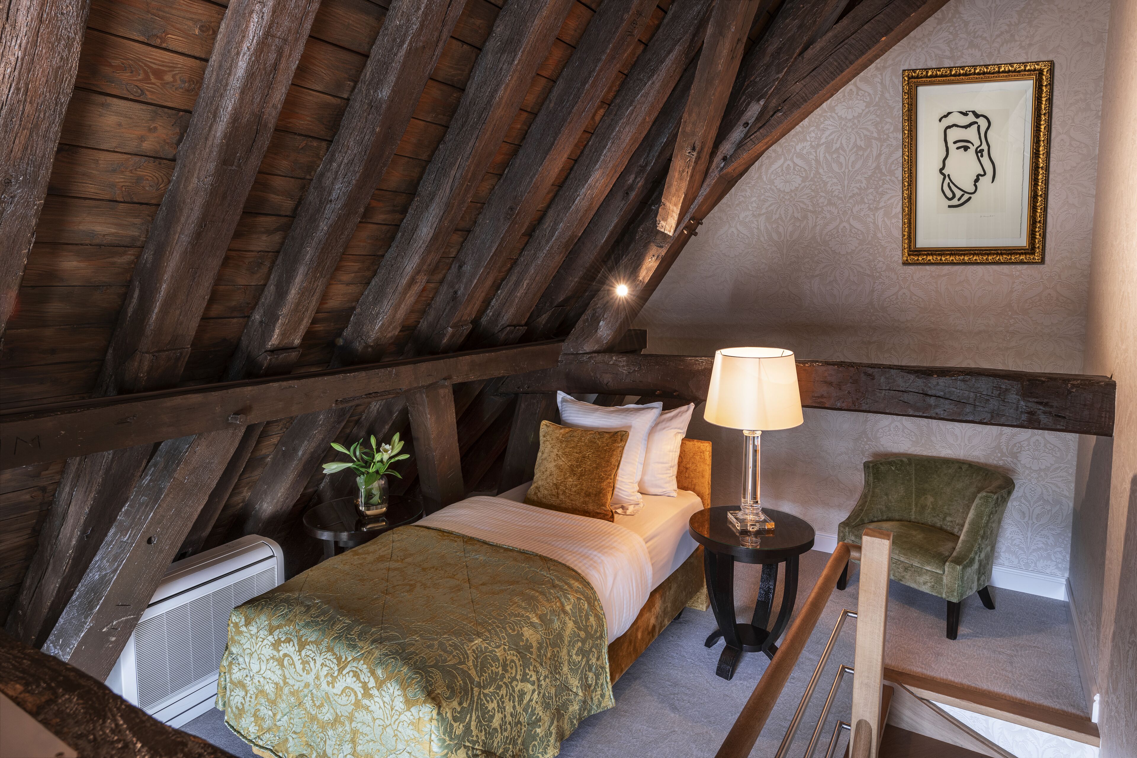 Un dormitorio con techo de madera, una cama con colcha verde, una mesita de noche con lámpara y una silla.