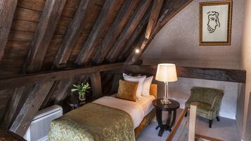 Un dormitorio con techo de madera, una cama con colcha verde, una mesita de noche con lámpara y una silla.