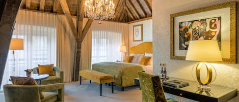 Quarto de hotel com uma cama, duas poltronas, uma escrivaninha e um lustre.