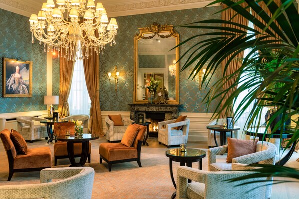A luxurious living room with a chandelier, comfortable seating, a fireplace, and a large mirror.