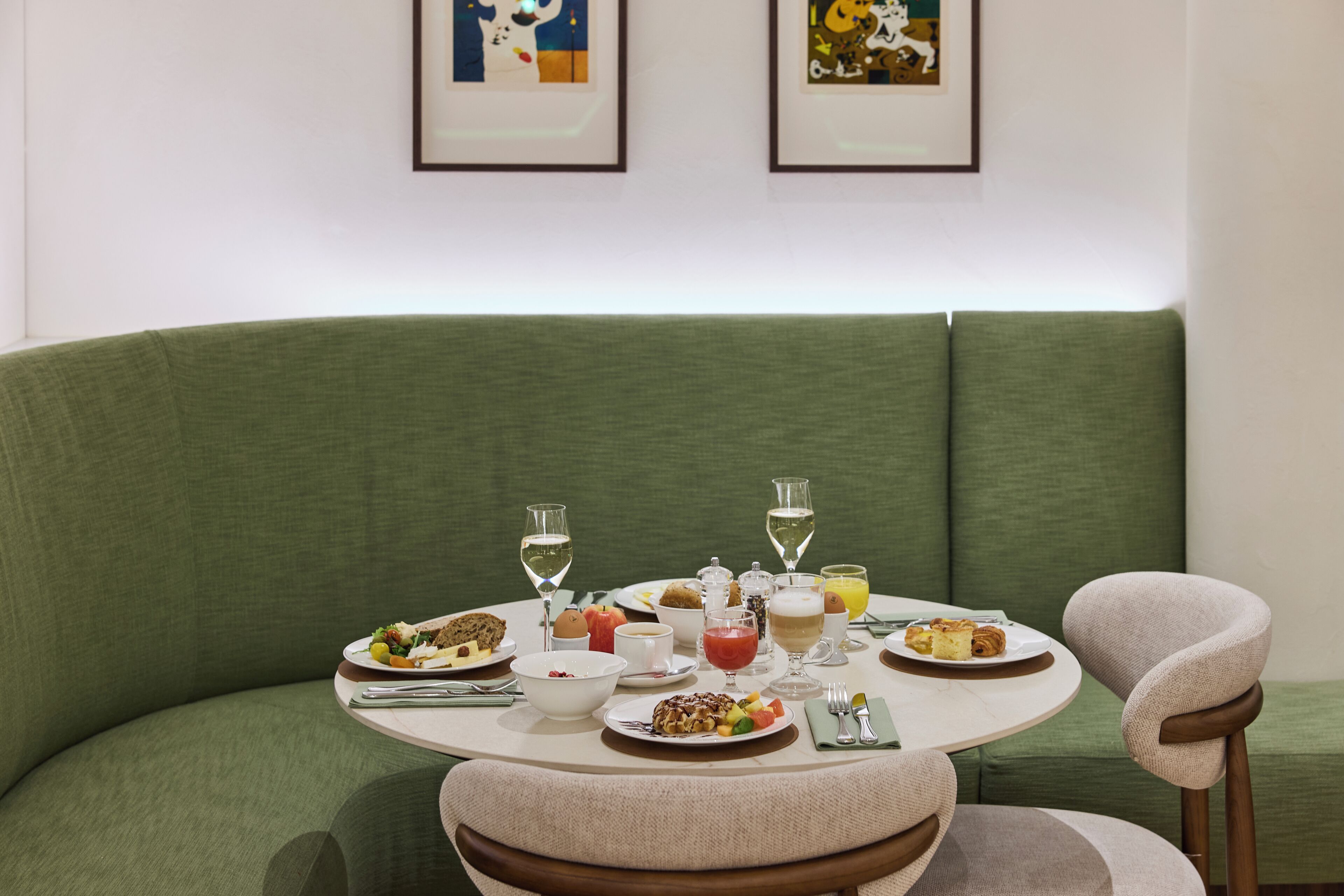 A dining area with a round table set for a meal, surrounded by green upholstered seating.