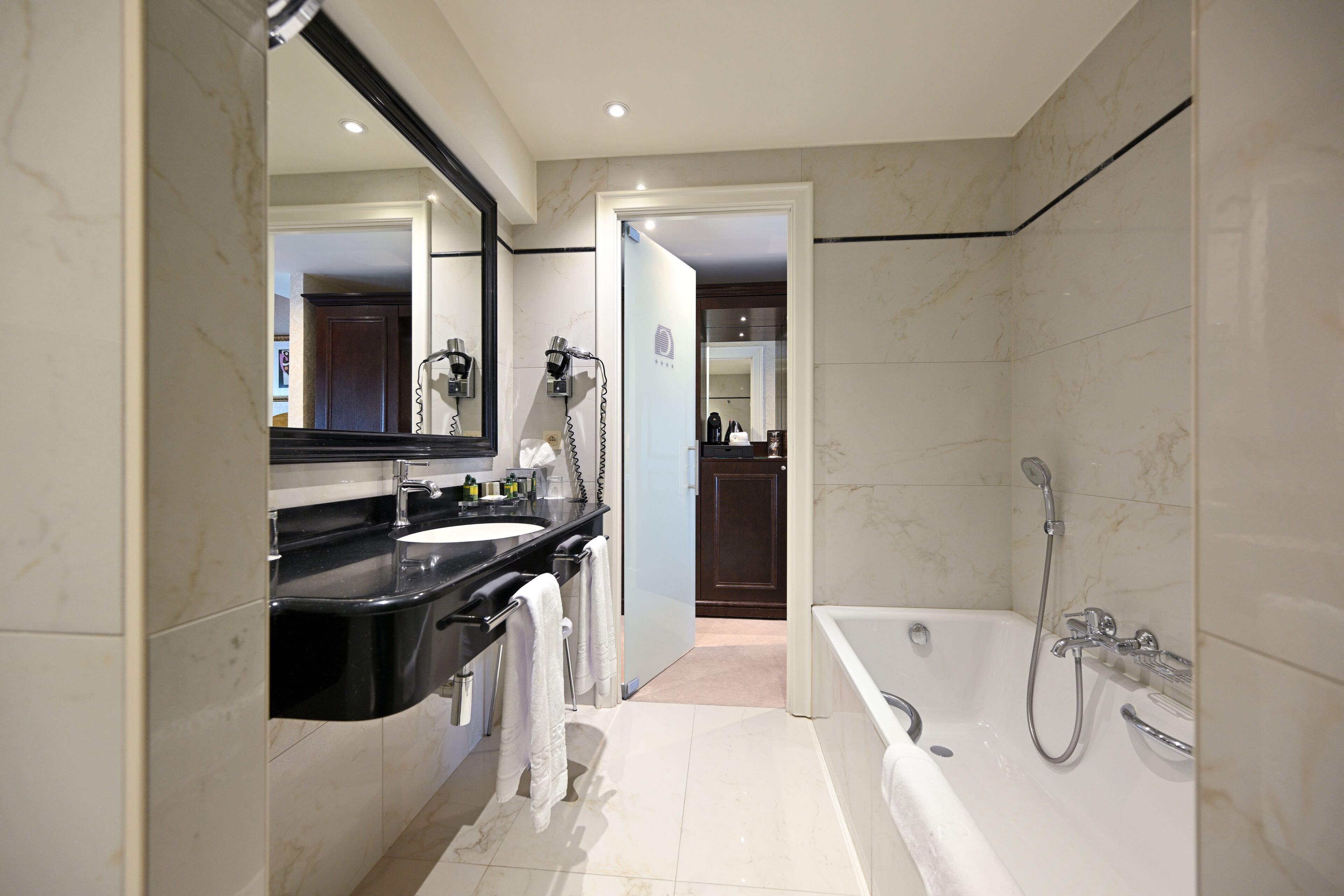 A modern bathroom with a large mirror, two sinks, a bathtub, and a shower.