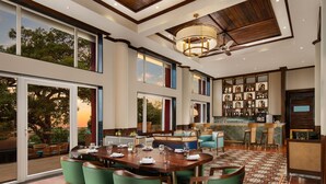 A spacious dining area with a large wooden table and green chairs, a bar area with stools, and a view of the outdoors through large windows. - Fountain, Mahabaleshwar - IHCL SeleQtions (Mahabaleshwar)