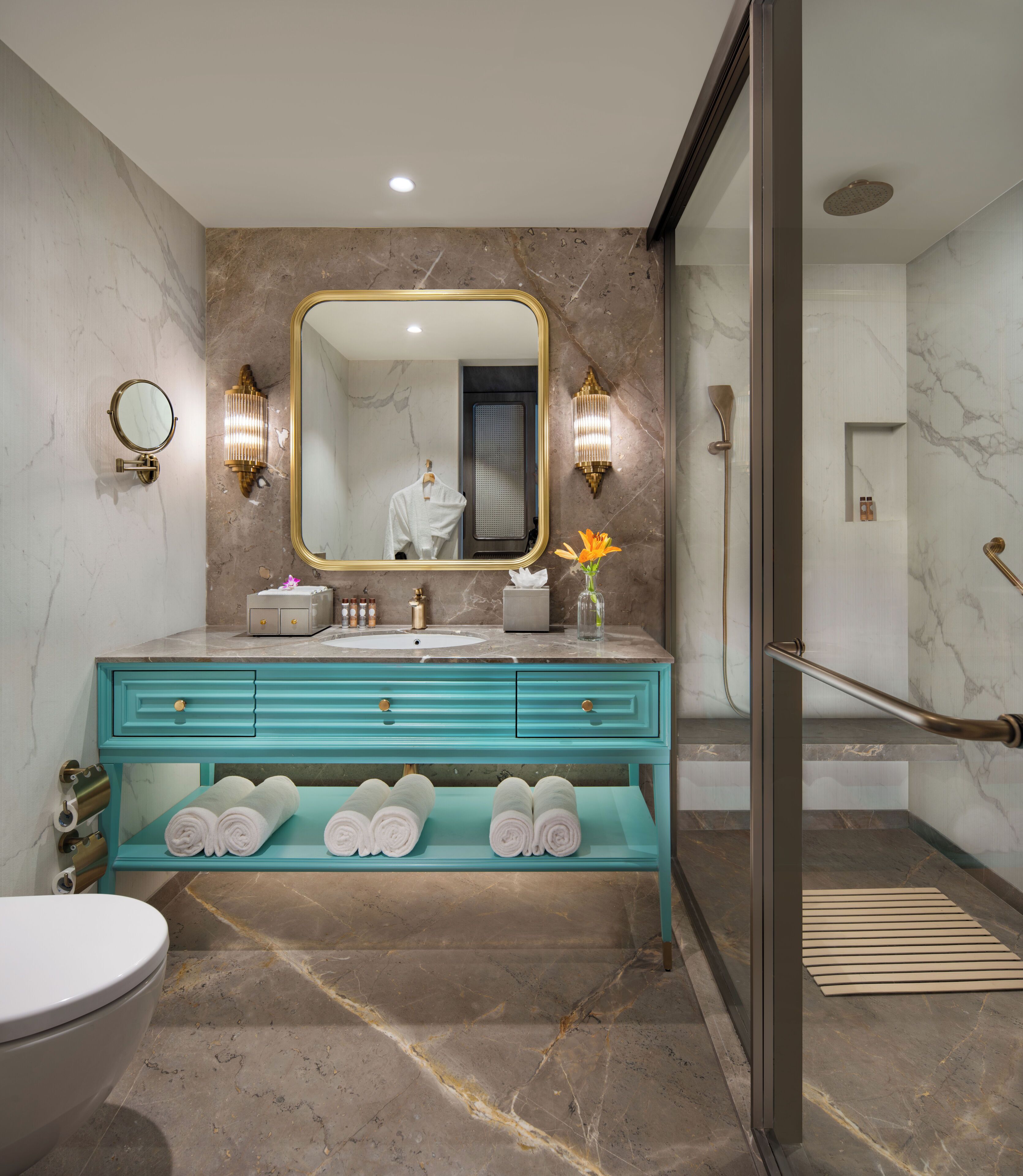 A modern bathroom with a marble floor, a turquoise vanity, a large mirror, and a glass shower enclosure.