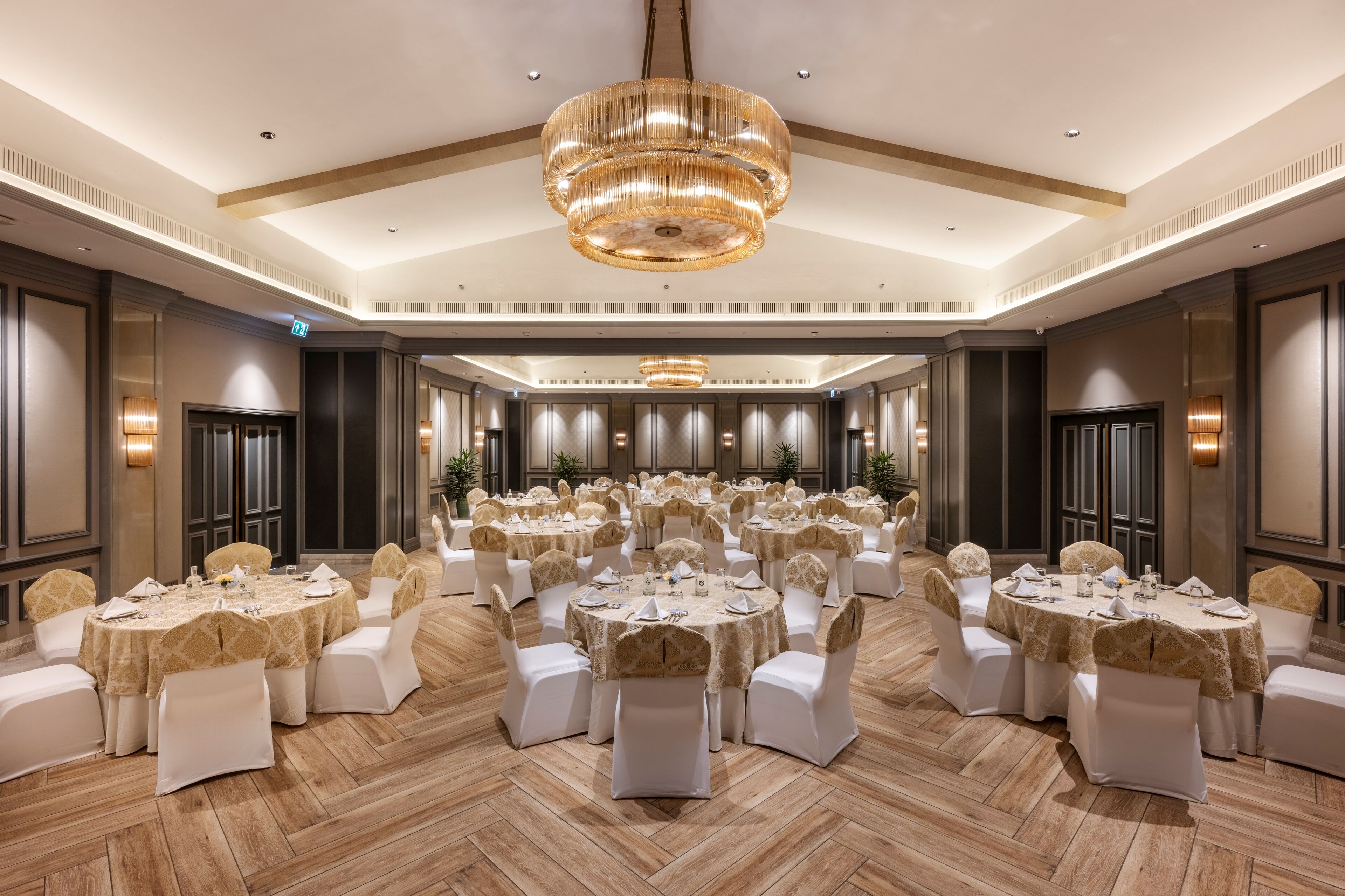 Un salón de banquetes con varias mesas redondas, sillas blancas y una lámpara de araña grande.