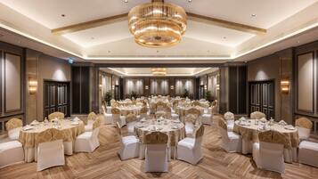 Un salón de banquetes con varias mesas redondas, sillas blancas y una lámpara de araña grande.