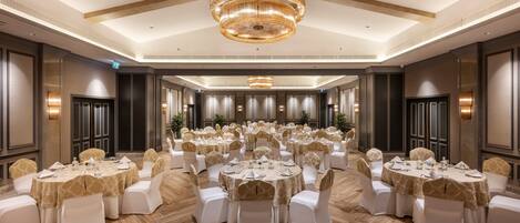 A banquet hall with multiple round tables, white chairs, and a large chandelier.