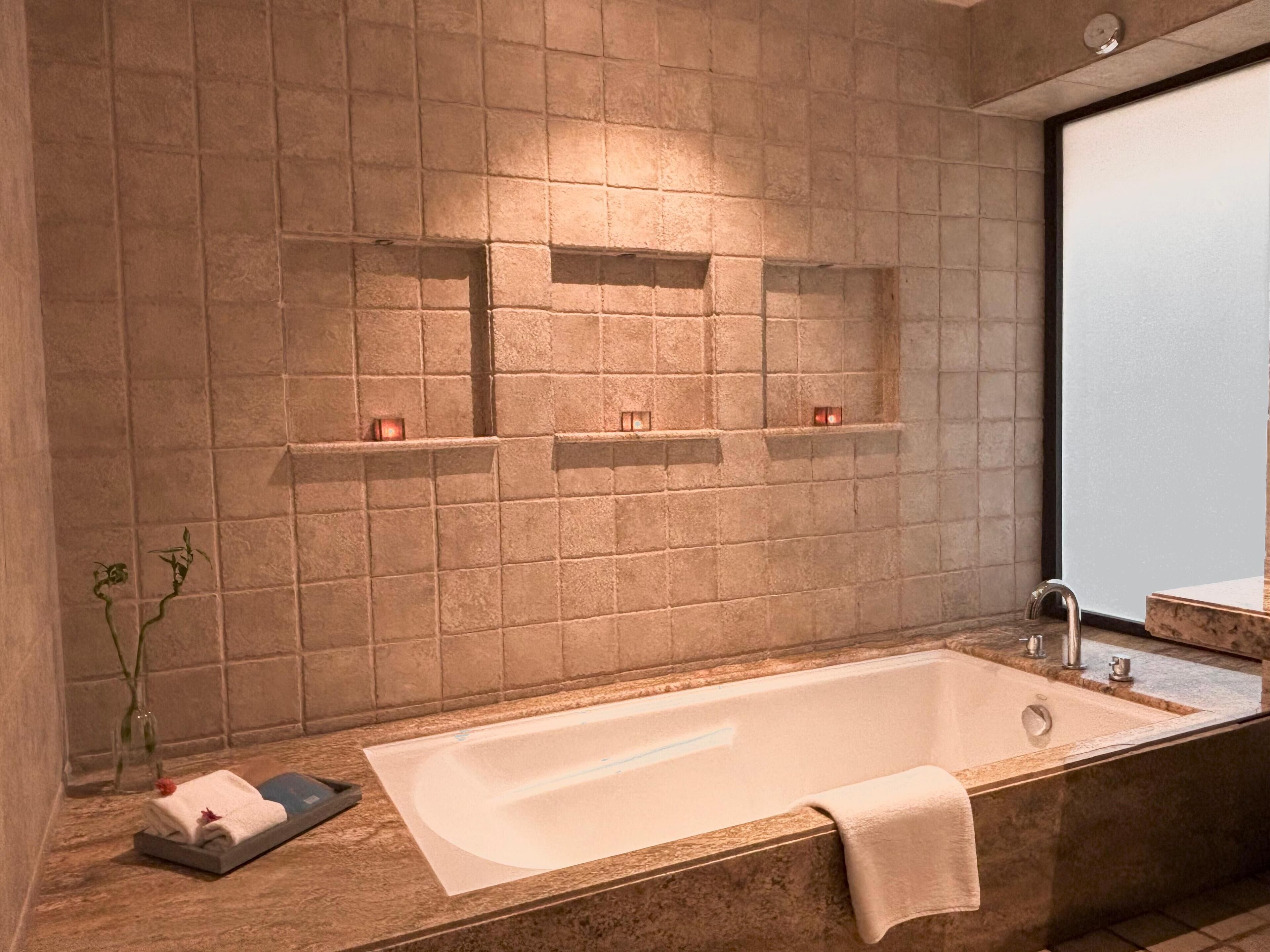 Een moderne badkamer met een vrijstaand bad, een grote spiegel en inbouwplanken met kaarsen.