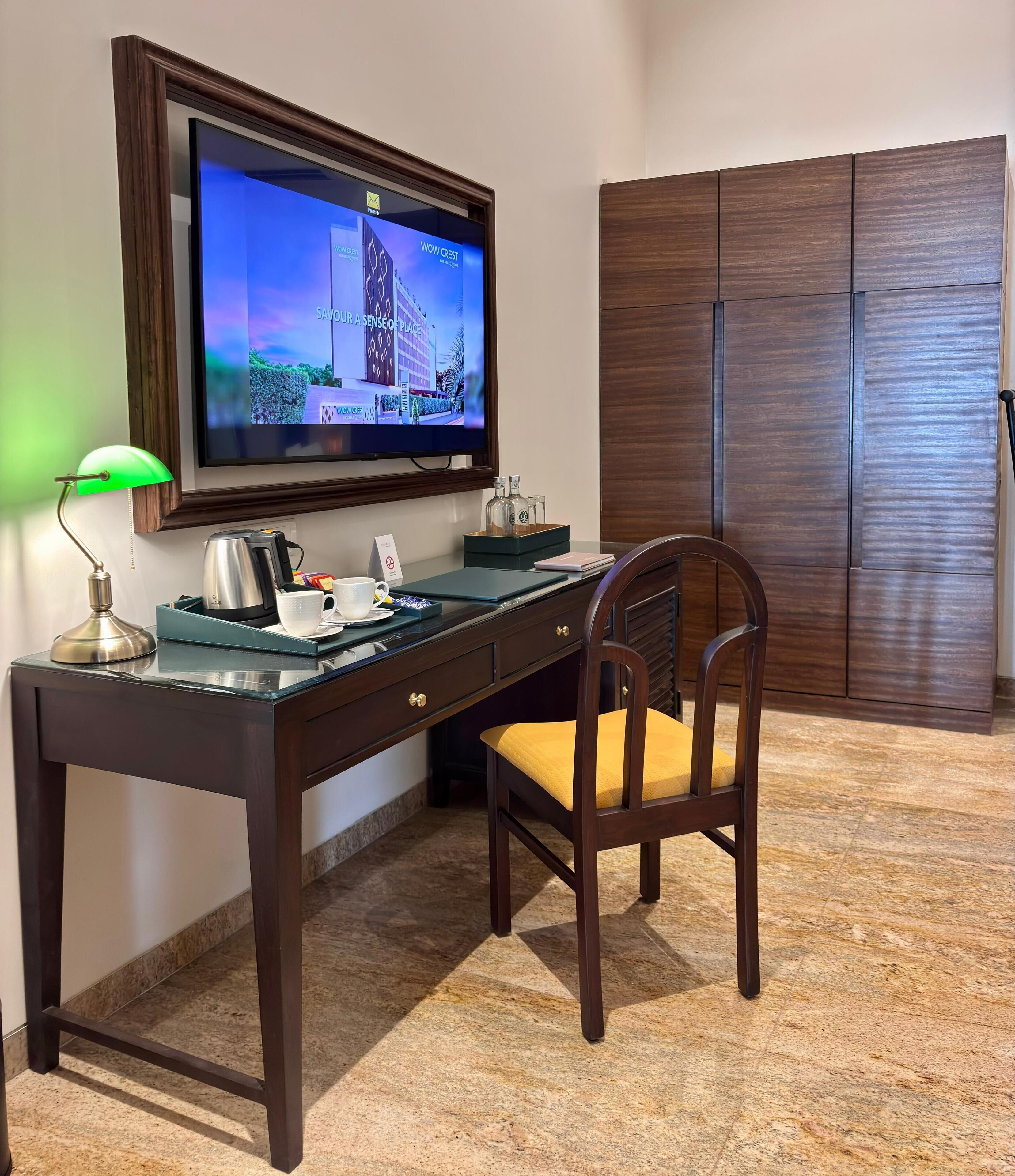 Ein Hotelzimmer mit Holzschreibtisch, Stuhl, Wandfernseher und Kleiderschrank.