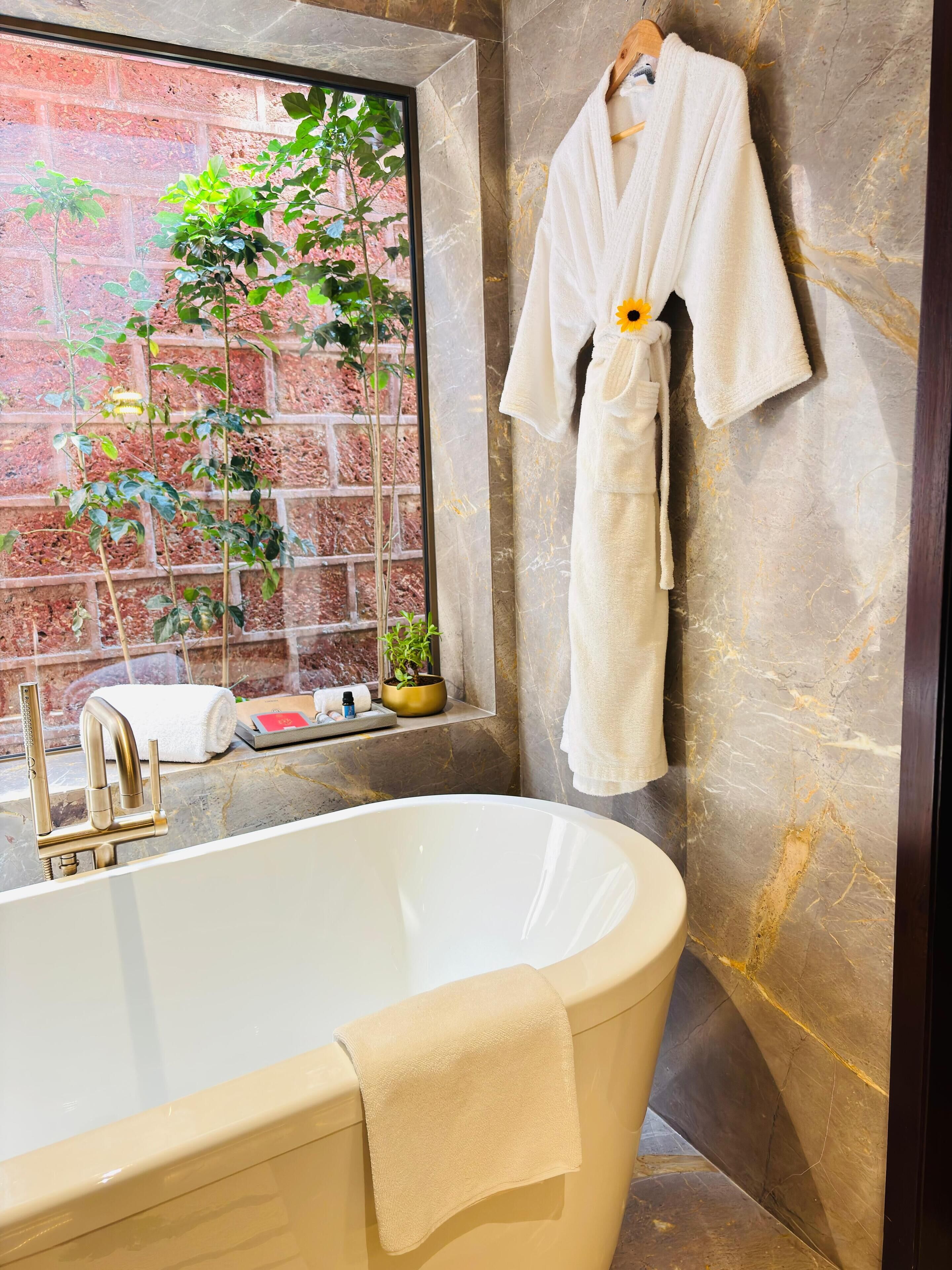 Une salle de bain avec une baignoire sur pieds, une fenêtre donnant sur un paysage verdoyant et un porte-serviettes avec une serviette blanche.