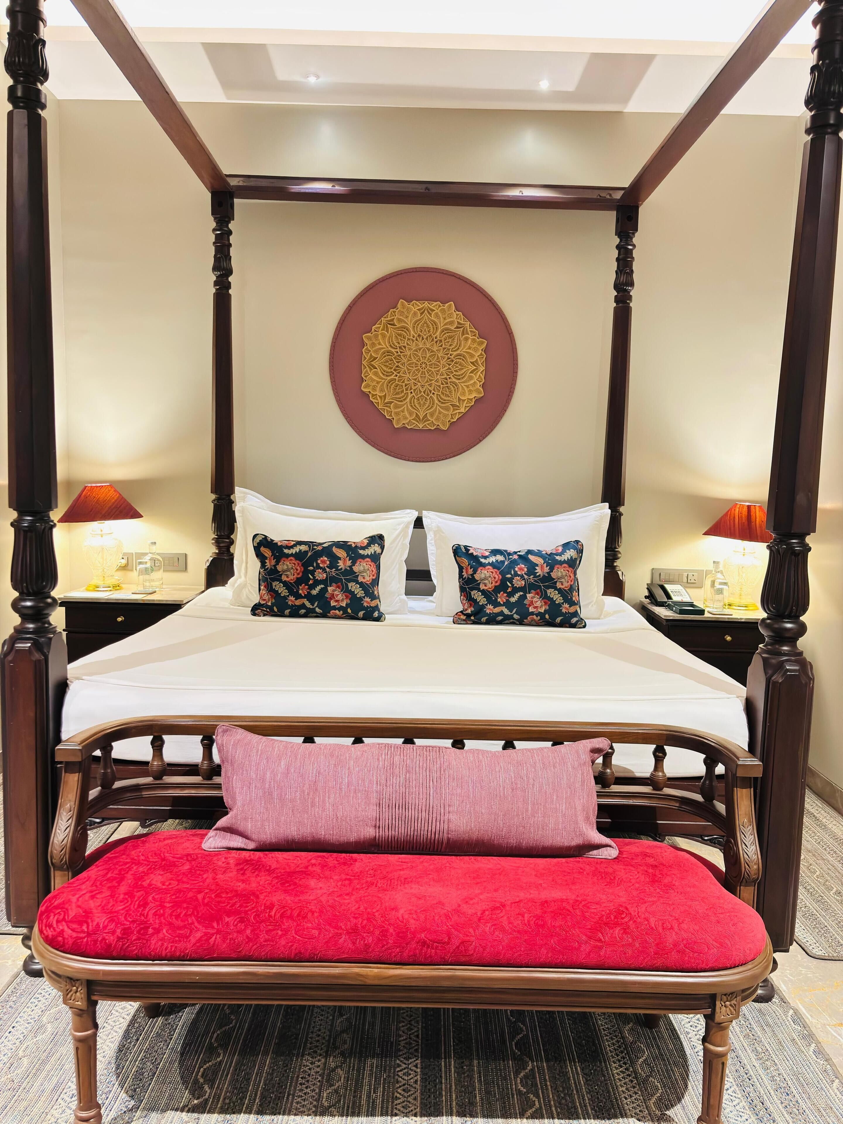 Una cama con dosel con un banco tapizado rojo, almohadas estampadas y un adorno mural.