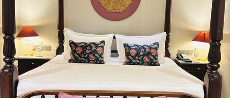 Una cama con dosel con un banco tapizado rojo, almohadas estampadas y un adorno mural.
