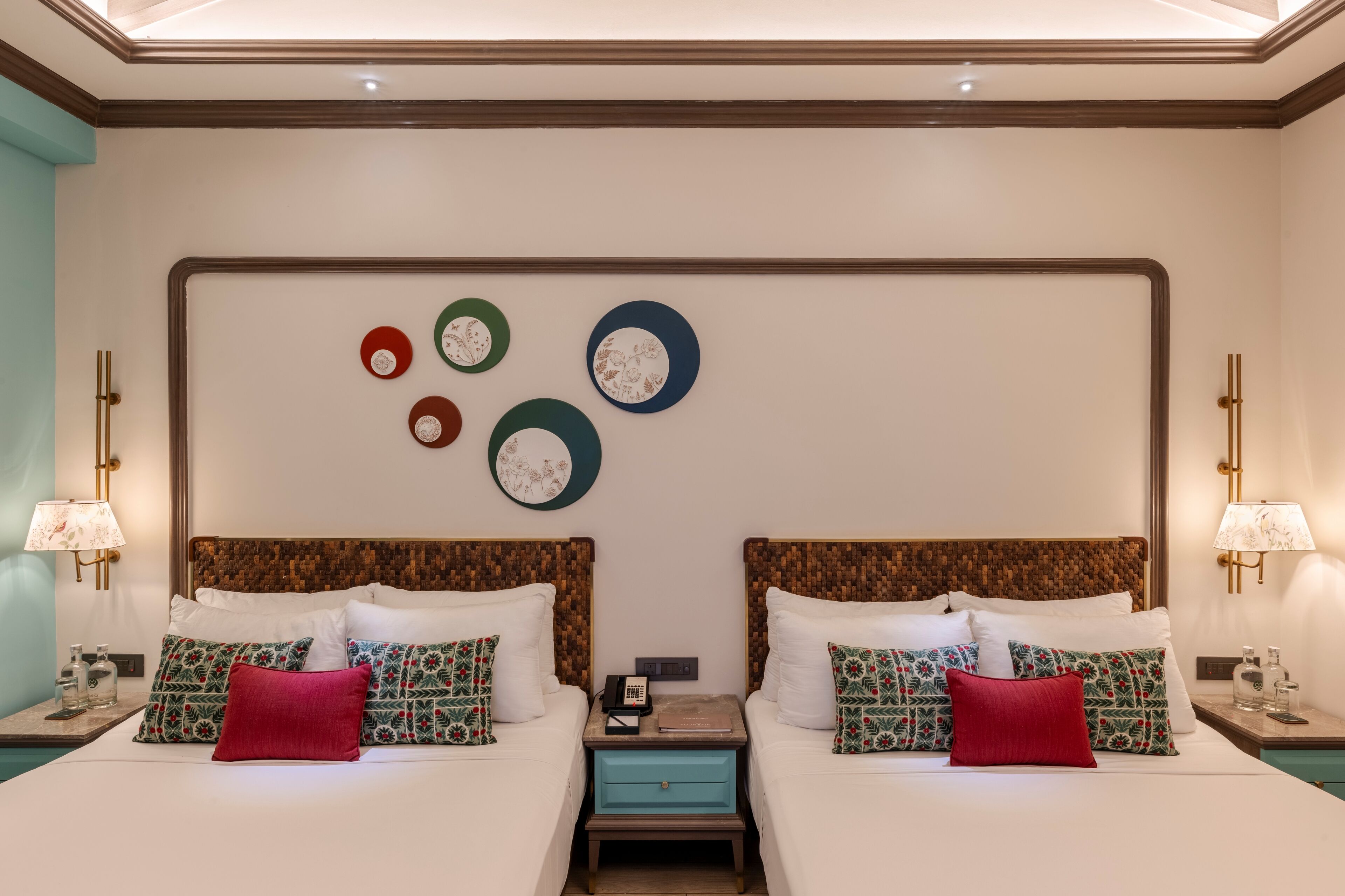 Habitación de hotel con dos camas, cada una con almohadas estampadas y una mesita de noche con lámpara y teléfono.