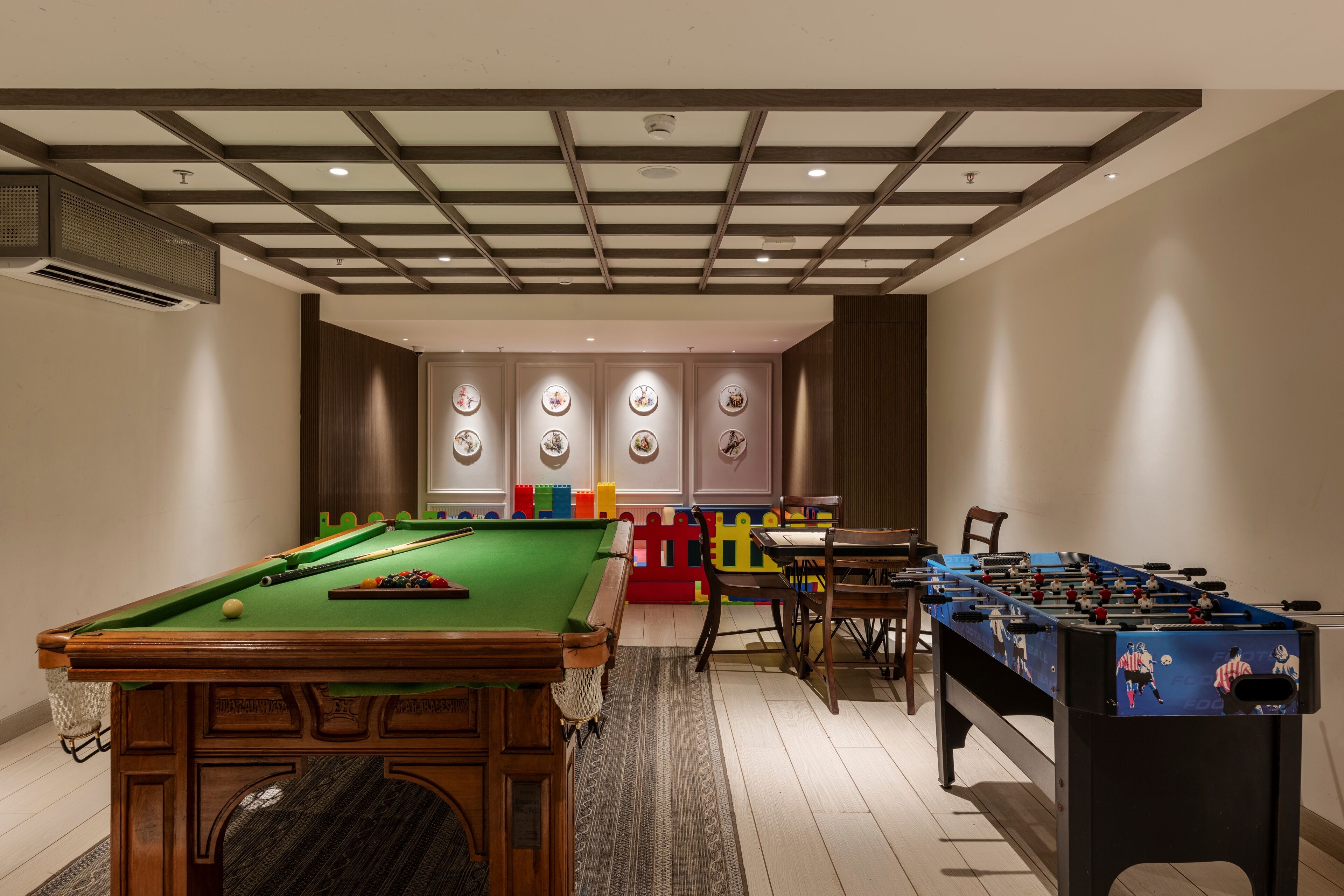 A room with a pool table, a foosball table, and a seating area with a table and chairs.